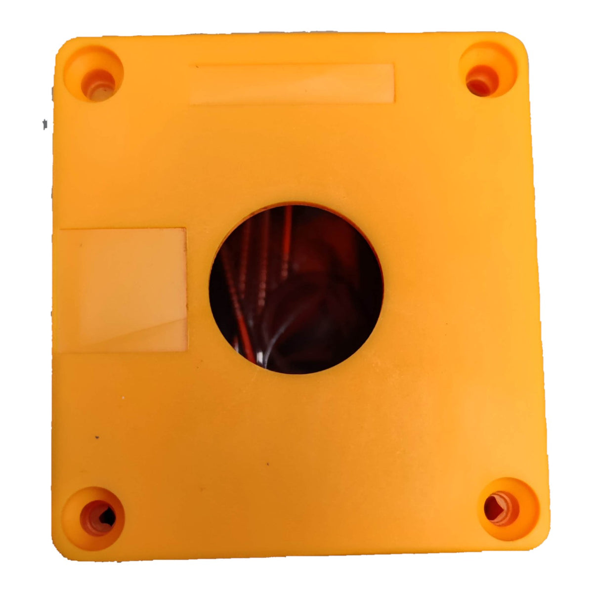 A square orange plastic component with four pre-drilled screw holes in the corners and a circular cutout in the center, showing dark internal wiring or channels. A small rectangular label area is visible on the top side.