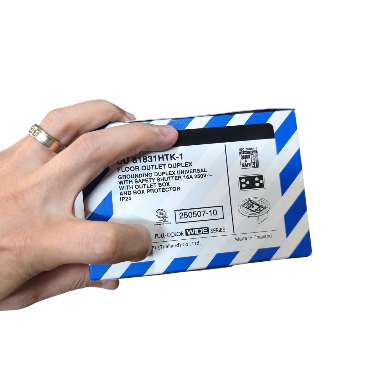 A hand holding a blue and white striped box of THOR Floor Outlet Duplex GFCI Outlet Universal, with product text and icons visible on the side.