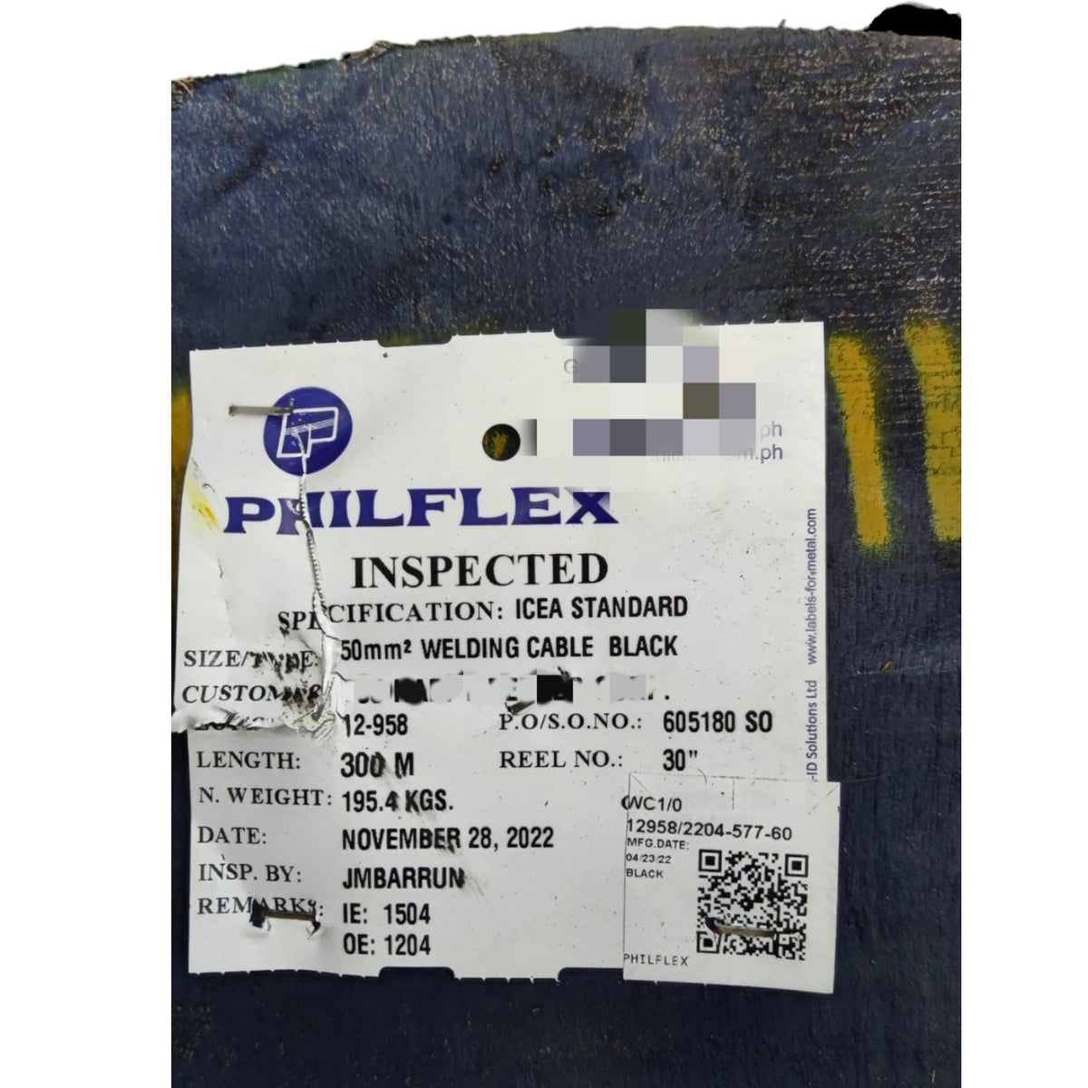A white paper inspection label for a Philflex welding cable reel, showing specifications and details, placed on a dark blue textured surface.