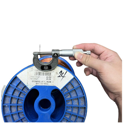 Hand holding a micrometer against a blue spool of wire on a white background