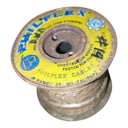 A vintage Philflex cable spool with a yellow and blue printed label, showing rusted metal edges and the brand name 'PHILFFLEX' printed on the top.