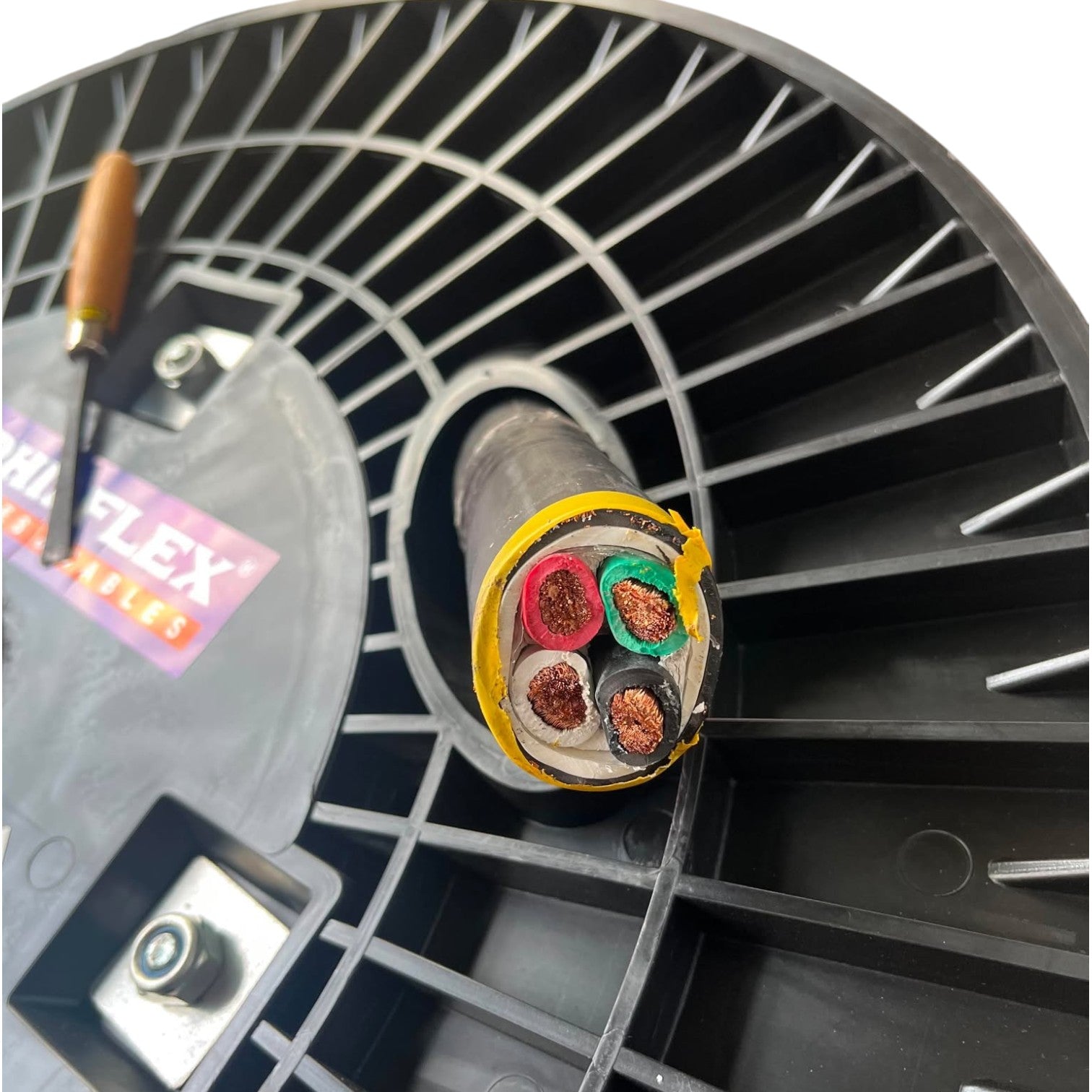 Close-up of a cable reel with multicolored wires and a tool on a black background