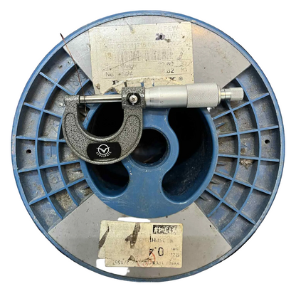 Micrometer on a blue metal spool with labels Phillflex 100 Grams Magnet Wire AWG 26 Enameled Copper Wire 0.40mm Heavy Formix Approx 82.65 Meters Per Roll Electx Electrical Supply