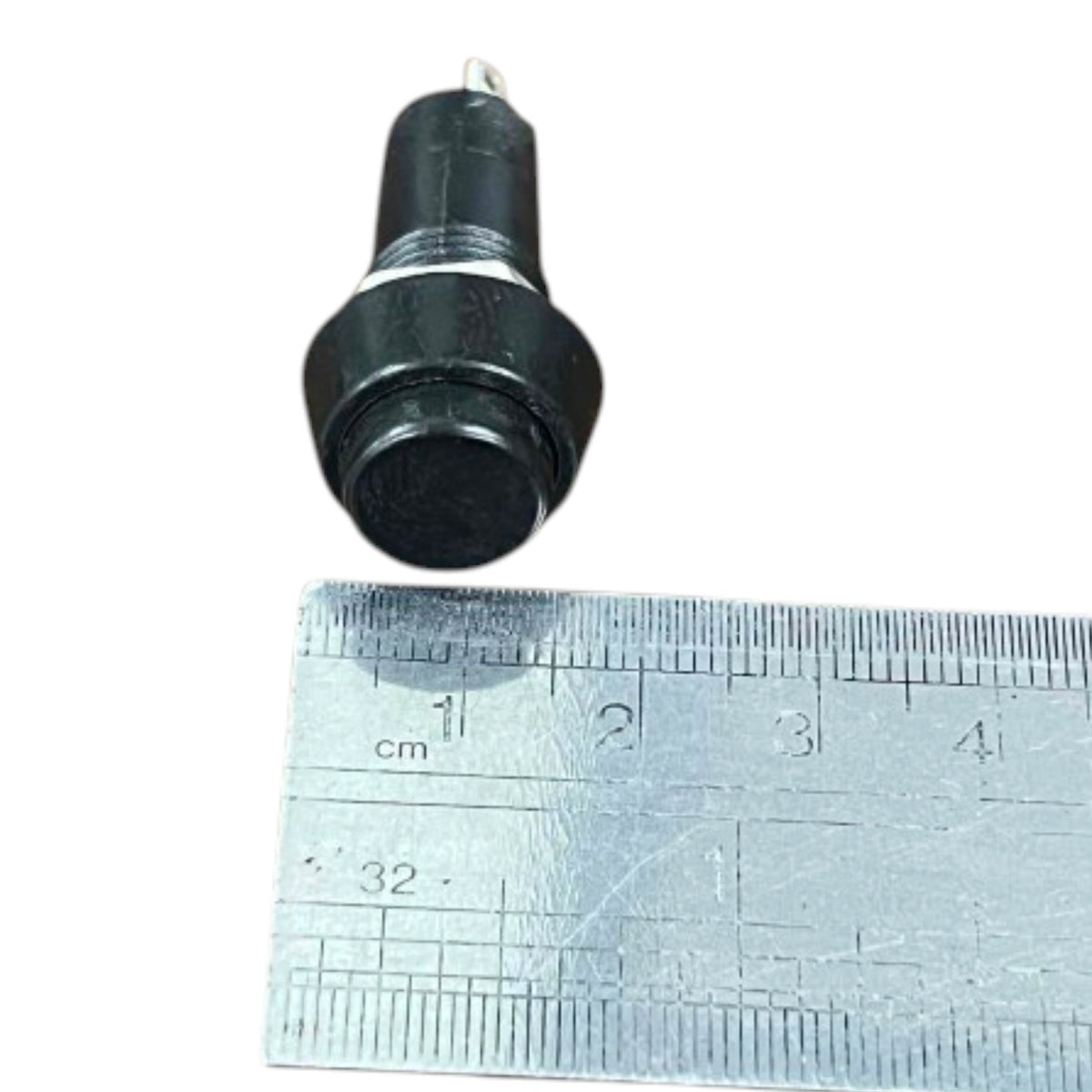 A small black cylindrical electrical push-button switch with a metal screw terminal and a round black button face, shown above a metal ruler for scale on a white background.