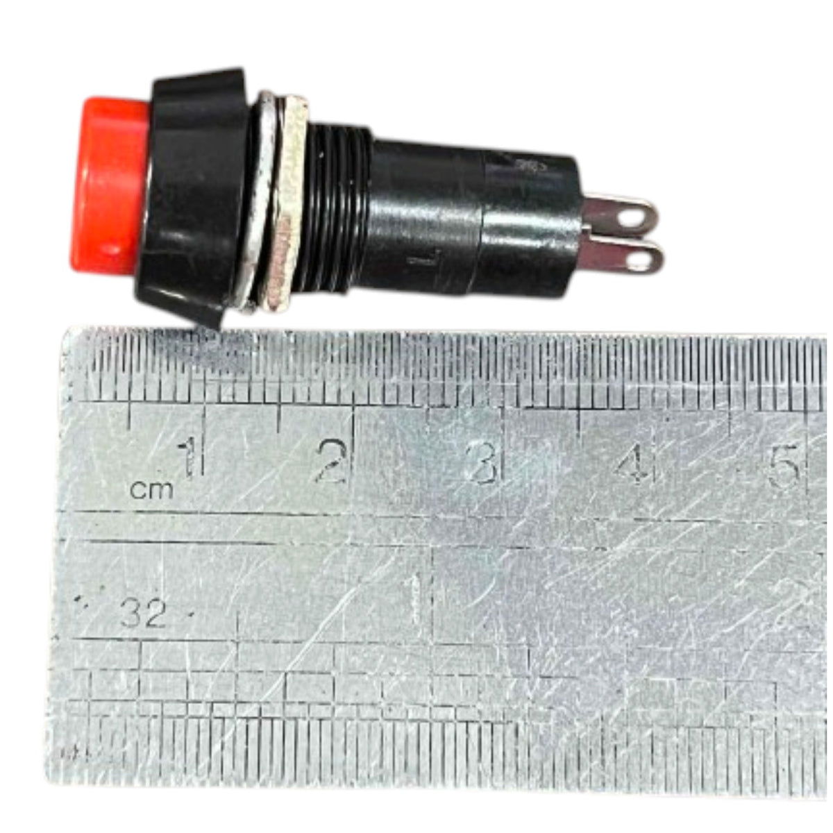 A small black electrical push-button with a red button head and two metal pins, shown above a metal ruler for scale on a white background.
