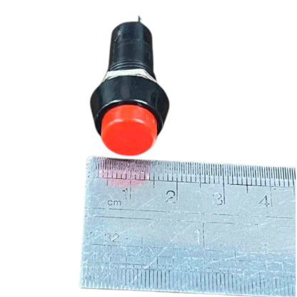 A small black and red push-button switch shown above a metal ruler for scale on a white background.