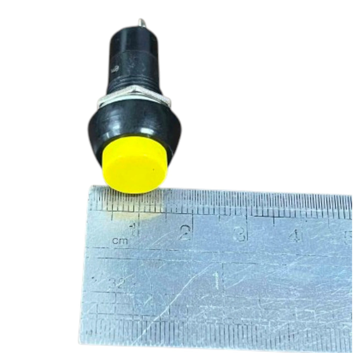 A small black electrical push-button with a bright yellow circular front, shown next to a metal ruler for scale on a white background.