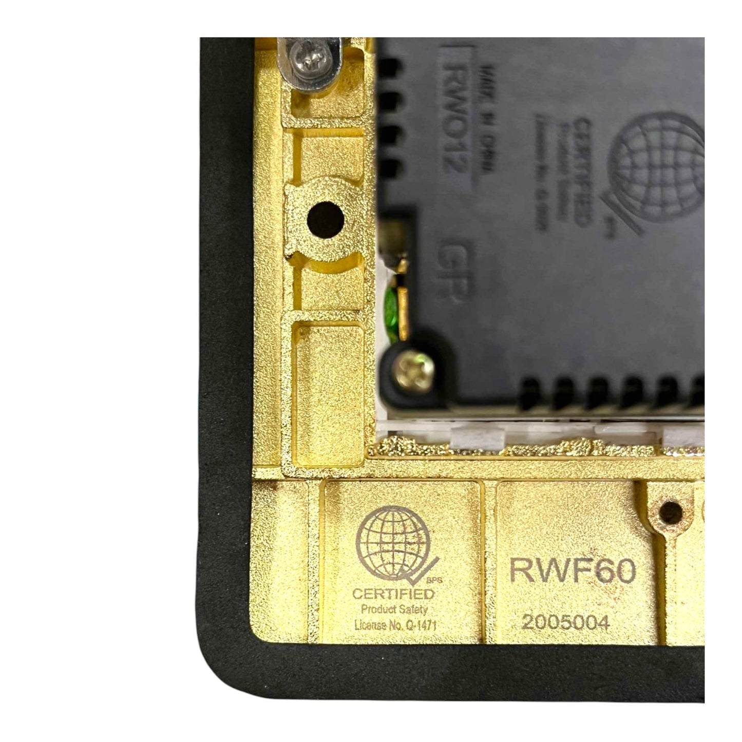 Close-up of the corner of a gold and black electronic device showing internal components, including a gold metal frame, a black circuit board, and certification text including 'RWF60' and 'Certified Product Safety'.