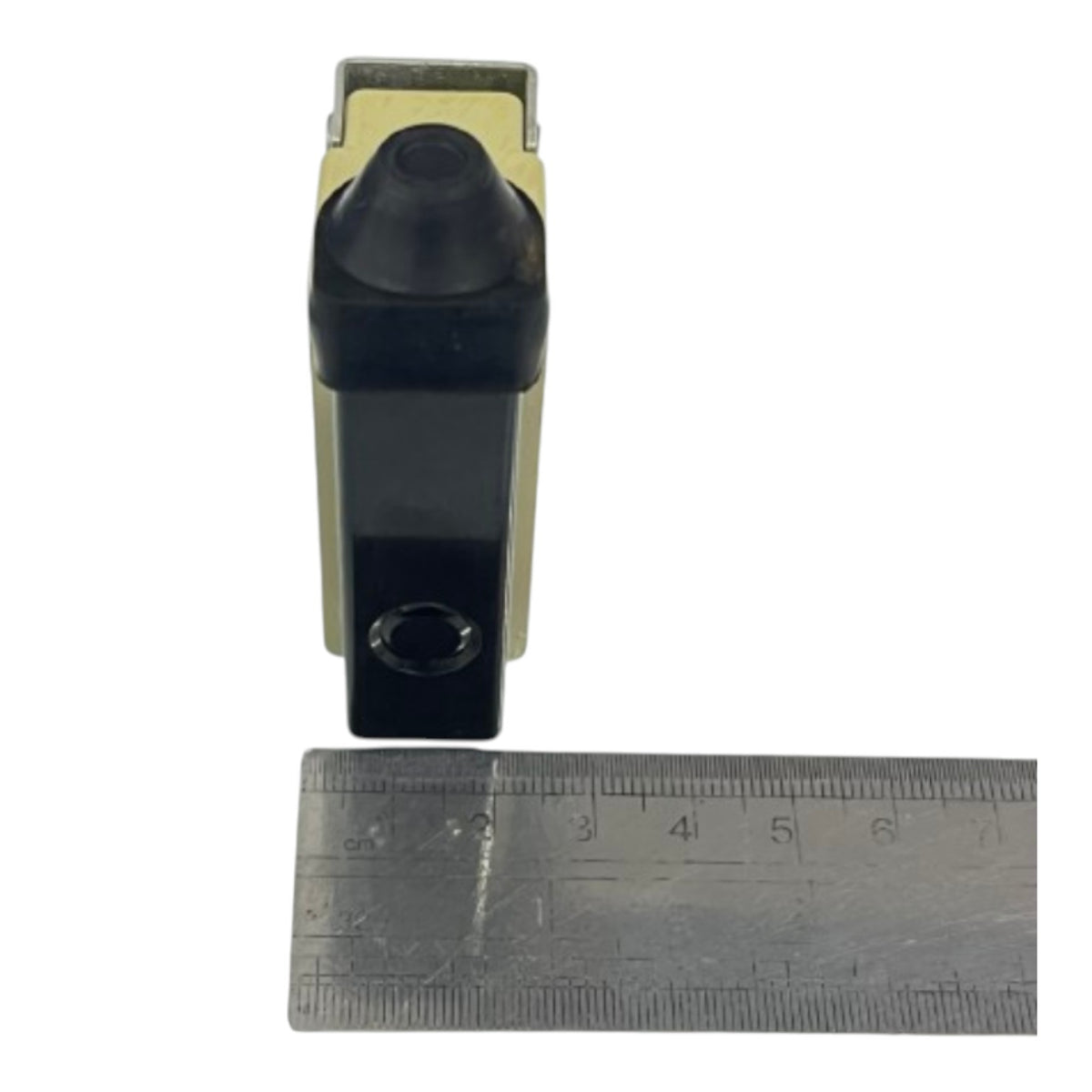 A small black and beige rectangular device with a rounded top and a circular opening on the front, shown next to a metal ruler for scale on a white background.