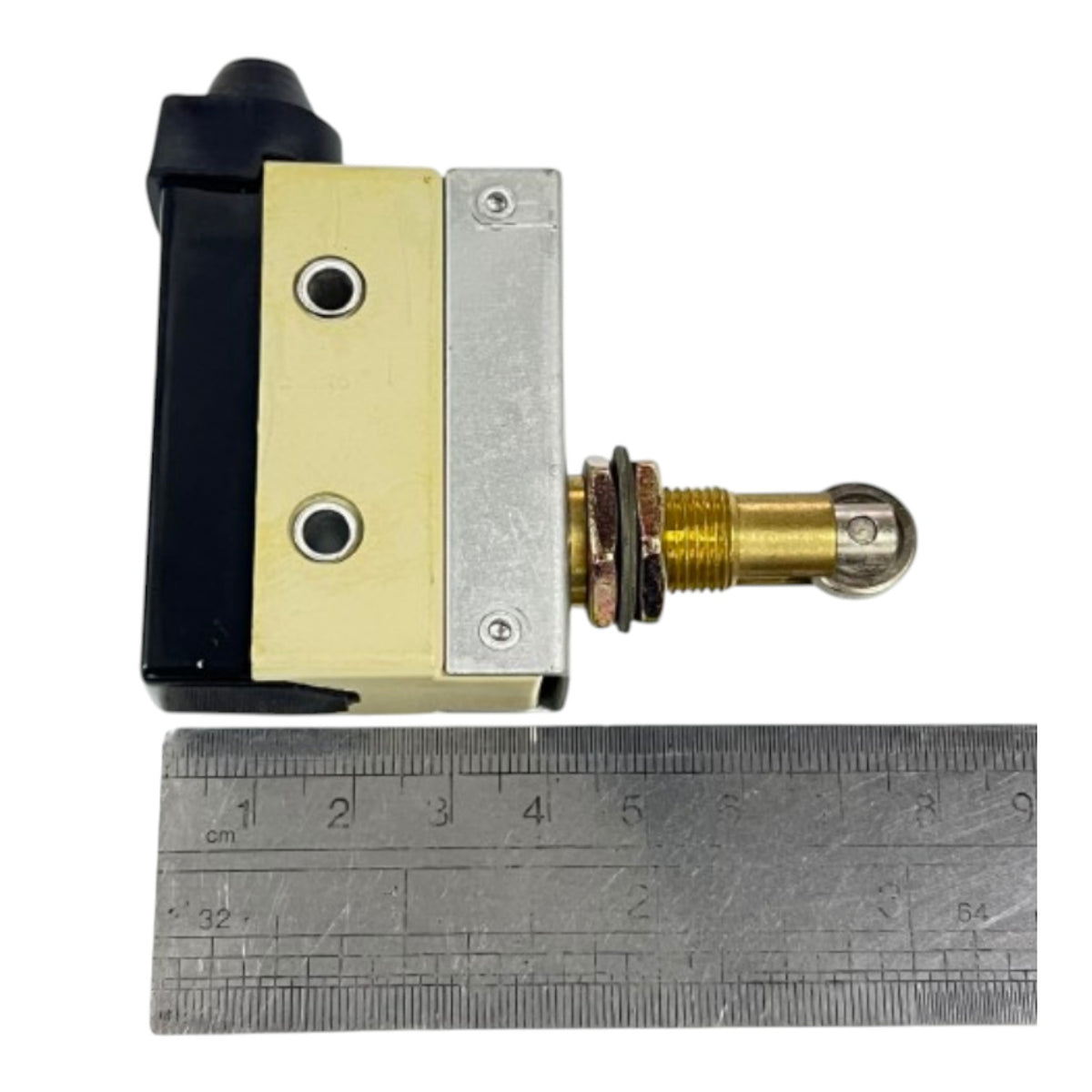 A small mechanical switch or valve component with a black and brass-colored body, shown next to a metal ruler for scale on a white background.