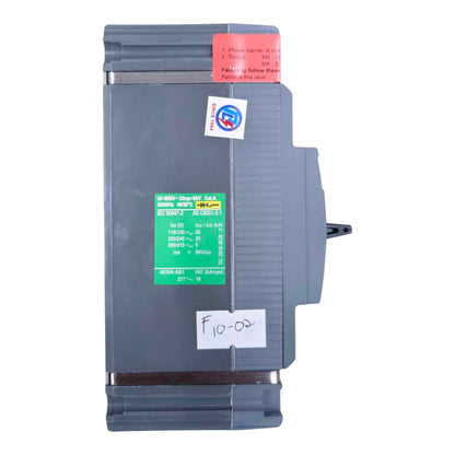 A gray industrial electrical component, likely a Siemens safety module, featuring a green technical specification sticker, a red warning label, and a white handwritten label on the front.