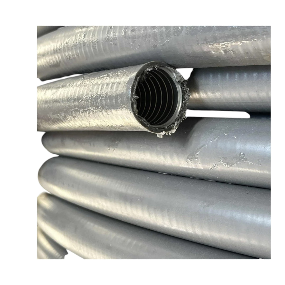 A close-up of stacked gray corrugated plastic pipes, with one pipe cut open to show the ribbed inner wall.