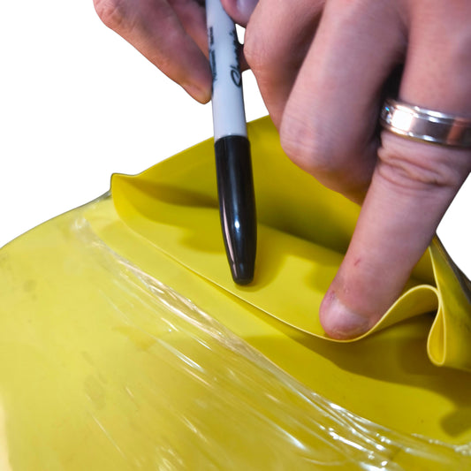 Person using a black marker on a yellow object with a white background