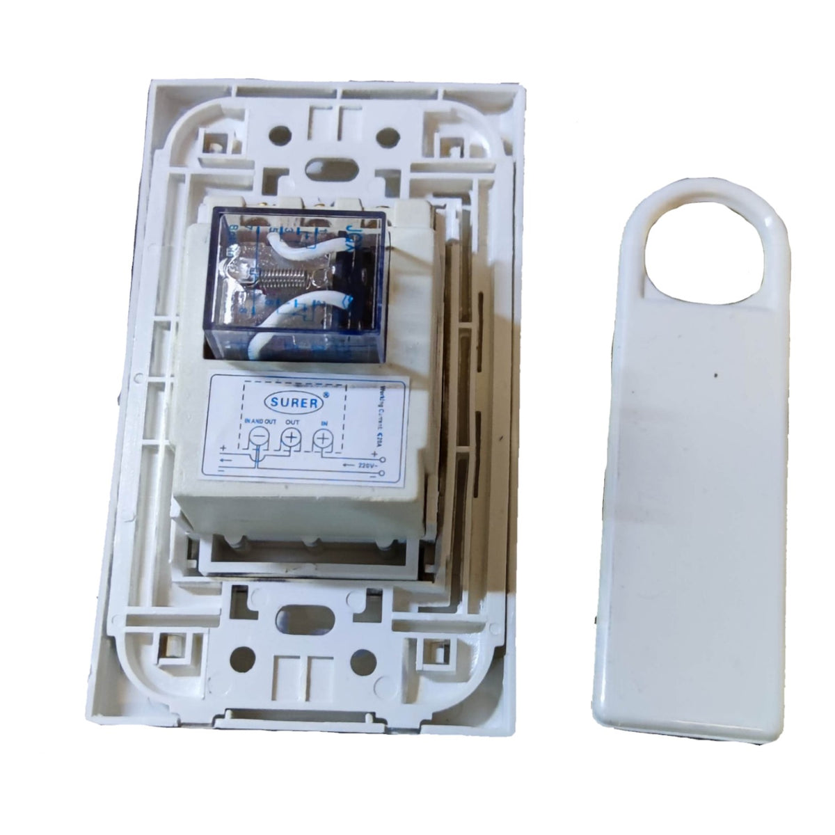 A white plastic electrical relay component shown open, revealing internal wiring and a small clear window, alongside a matching white plastic cover piece on a plain white background.