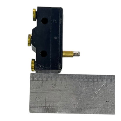 A small black mechanical switch or sensor with brass-colored screws and a protruding metal rod, shown above a metal ruler for scale on a white background.