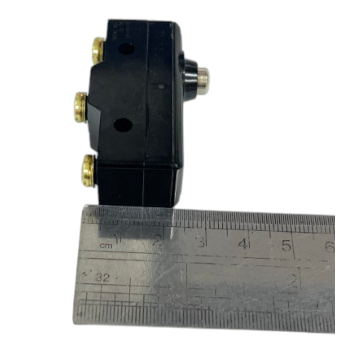 A small black electrical component with brass screw terminals, shown next to a metal ruler for scale on a white background.