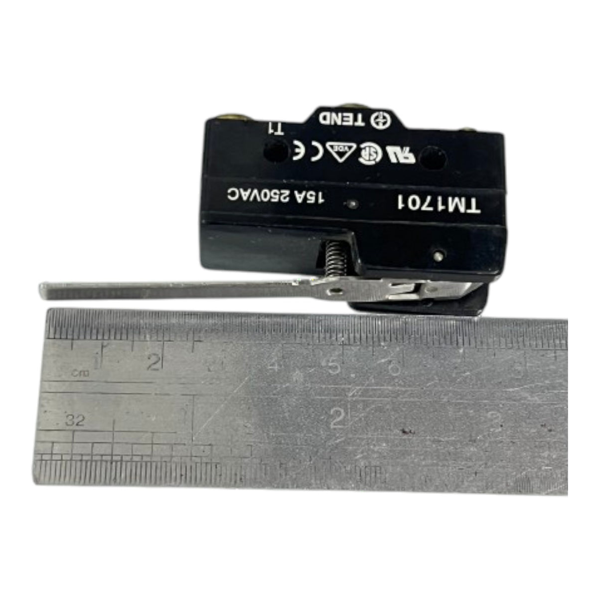 A black electrical contact switch with white printed specifications, shown next to a metal ruler for scale on a white background.