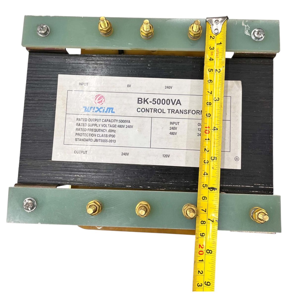 A 240V/120V control transformer with a black ribbed core, green metal end plates, and brass terminal screws, shown with a yellow tape measure indicating its dimensions.