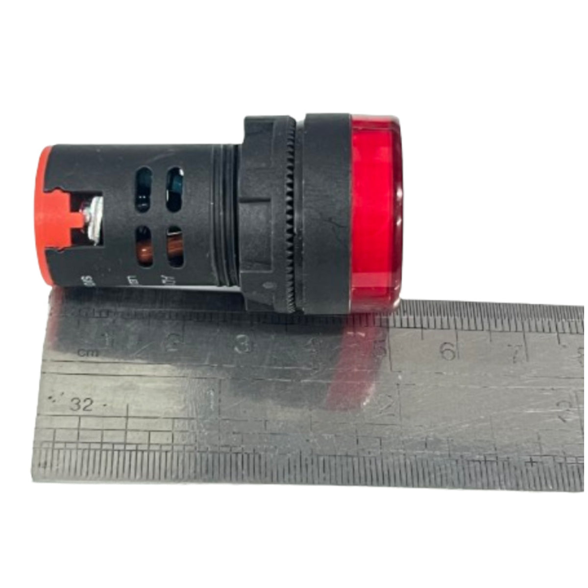 A small cylindrical electrical component with a black body, red end caps, and a transparent red lens, shown resting on top of a metal ruler against a white background.