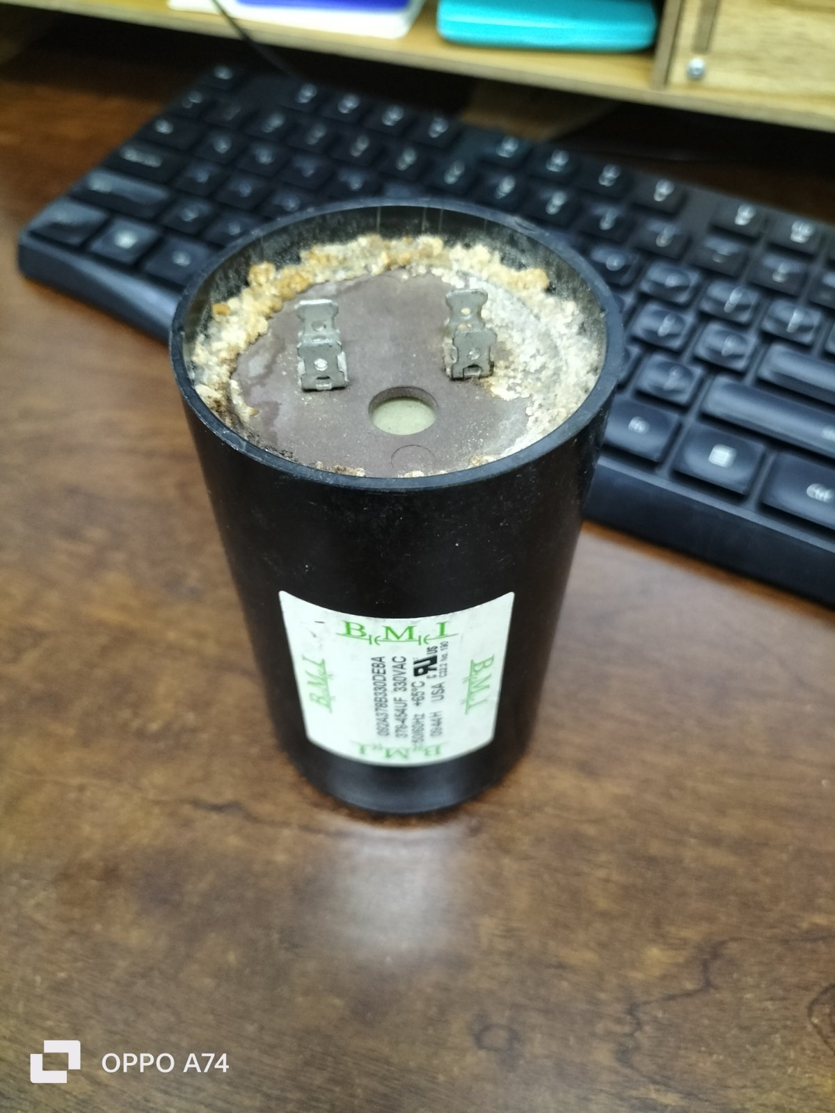 BMI starting capacitor 378-454UF black cylindrical electrical part on wooden desk near keyboard