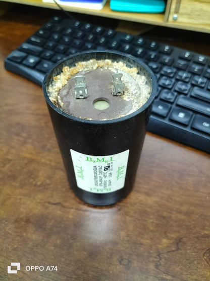 BMI starting capacitor 378-454UF black cylindrical electrical part on wooden desk near keyboard