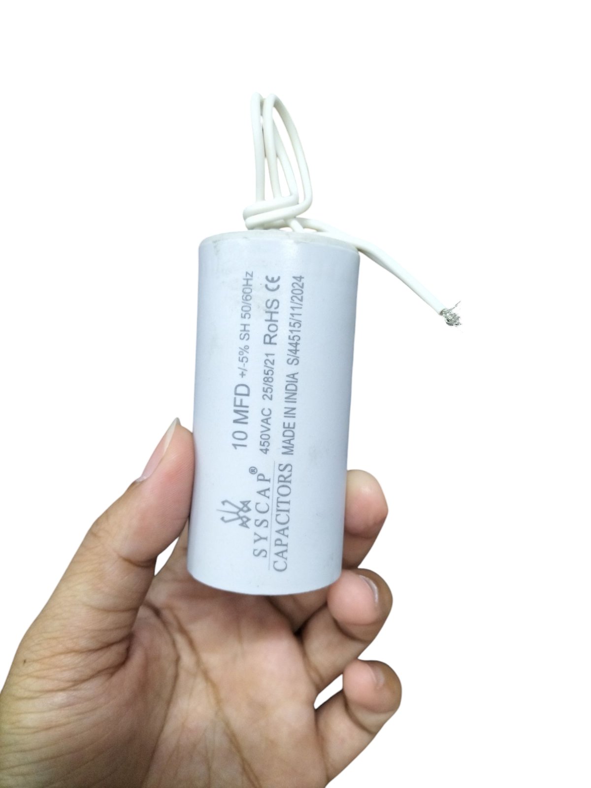 Hand holding a Syscap 10MFD 450 VAC Running Capacitor with white casing and wires