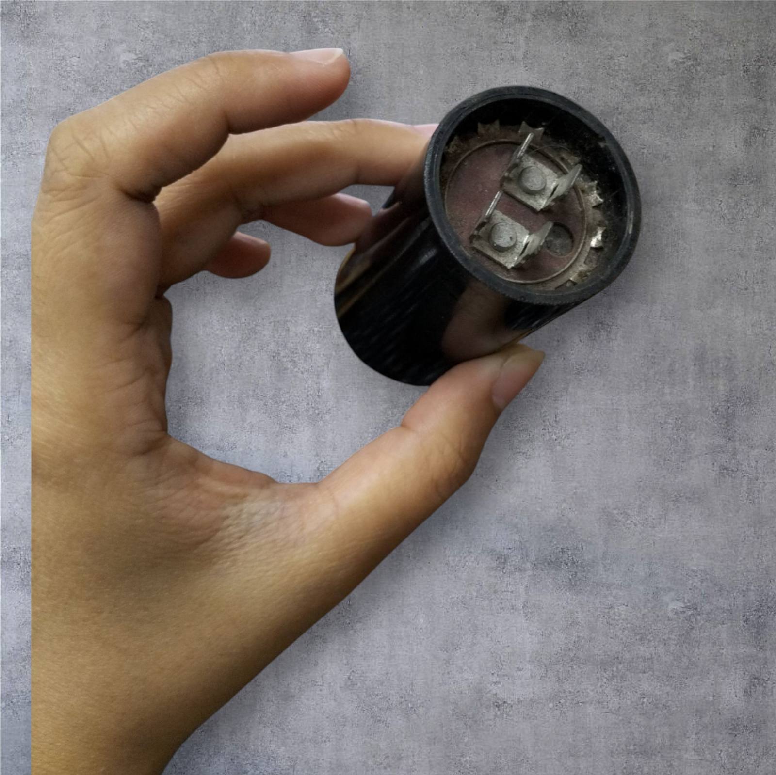 CDE electrical capacitor 110-125V held in hand, showcasing its compact design and connection terminals