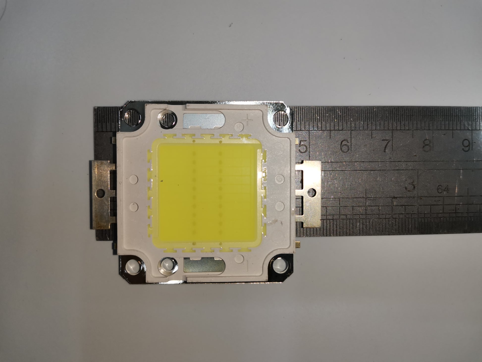 20w high power LED chip mounted on a white square base with metal connectors and ruler for size reference
