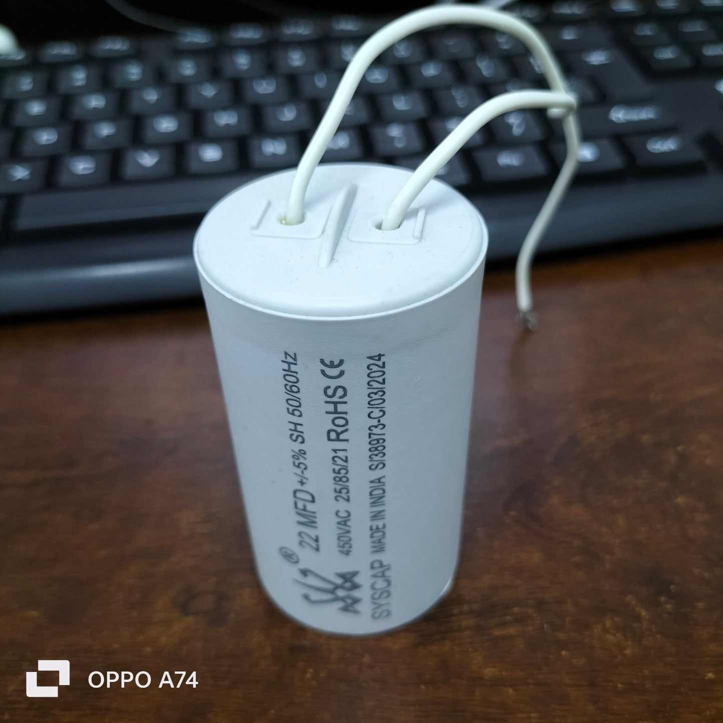 Syscap motor capacitor with white cylindrical body and attached wires