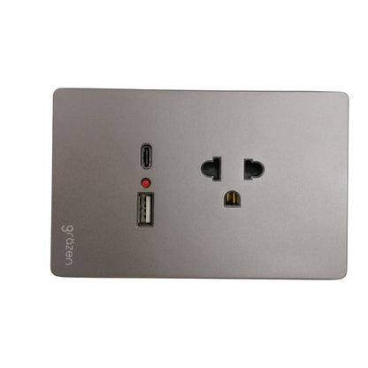 A square wall power adapter or charging dock with a brushed silver metal faceplate, featuring a USB-C port, a USB-A port, a small red indicator light, and a US-style outlet on a white background.