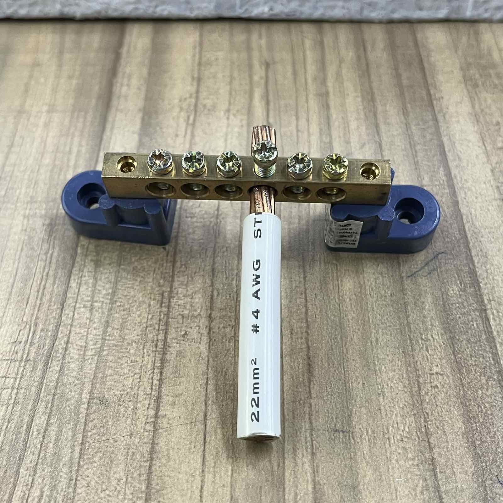 Grippes Grounding Bus Bars 4 Holes with screws and attached copper wire on wooden surface