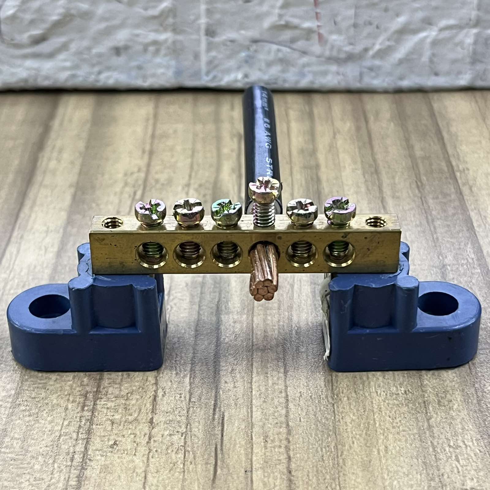 Grippes grounding bus bars 4 holes with mounted copper wire and blue mounting brackets on wooden surface