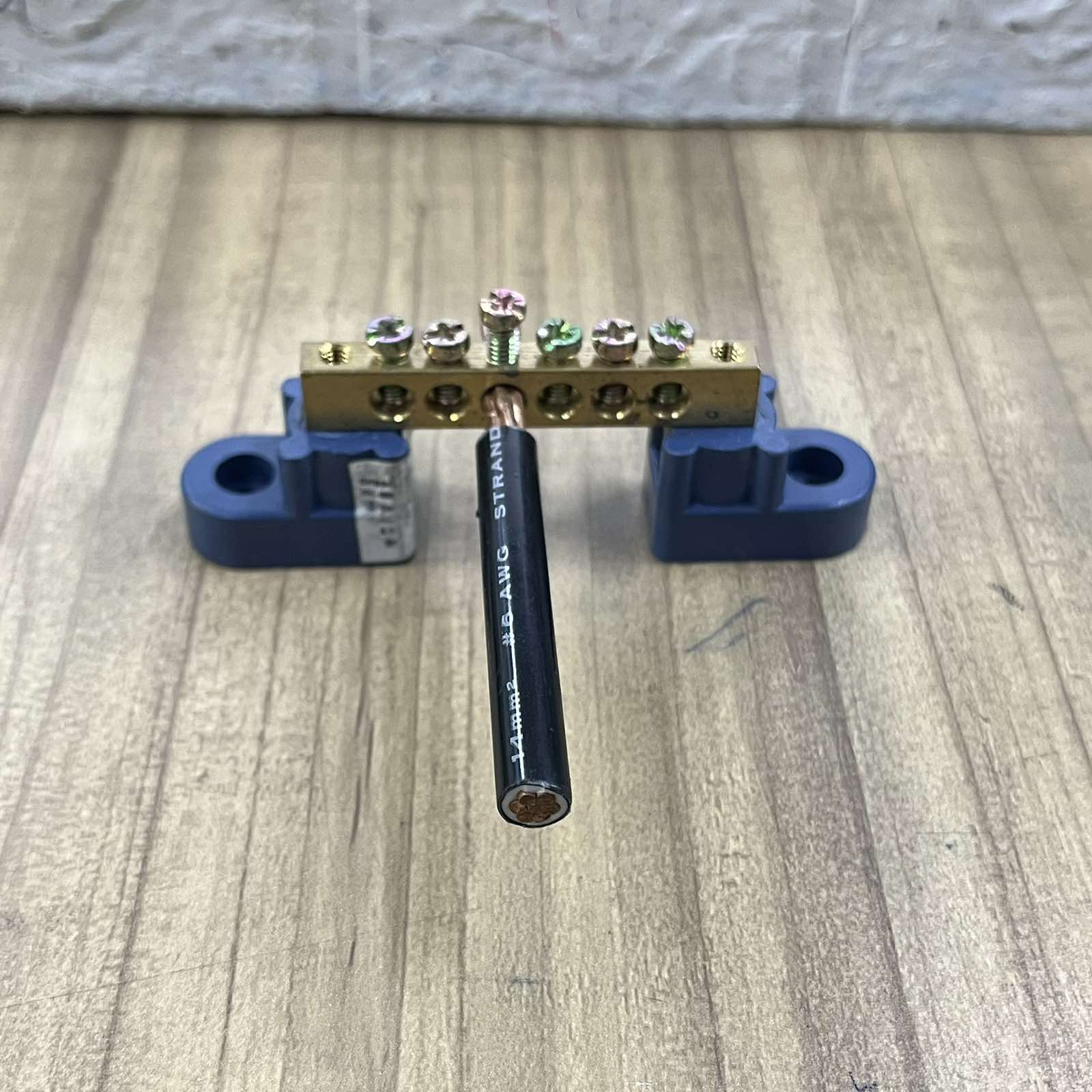 Grippes Grounding Bus Bars 4 Holes mounted with black electrical wire on wooden surface