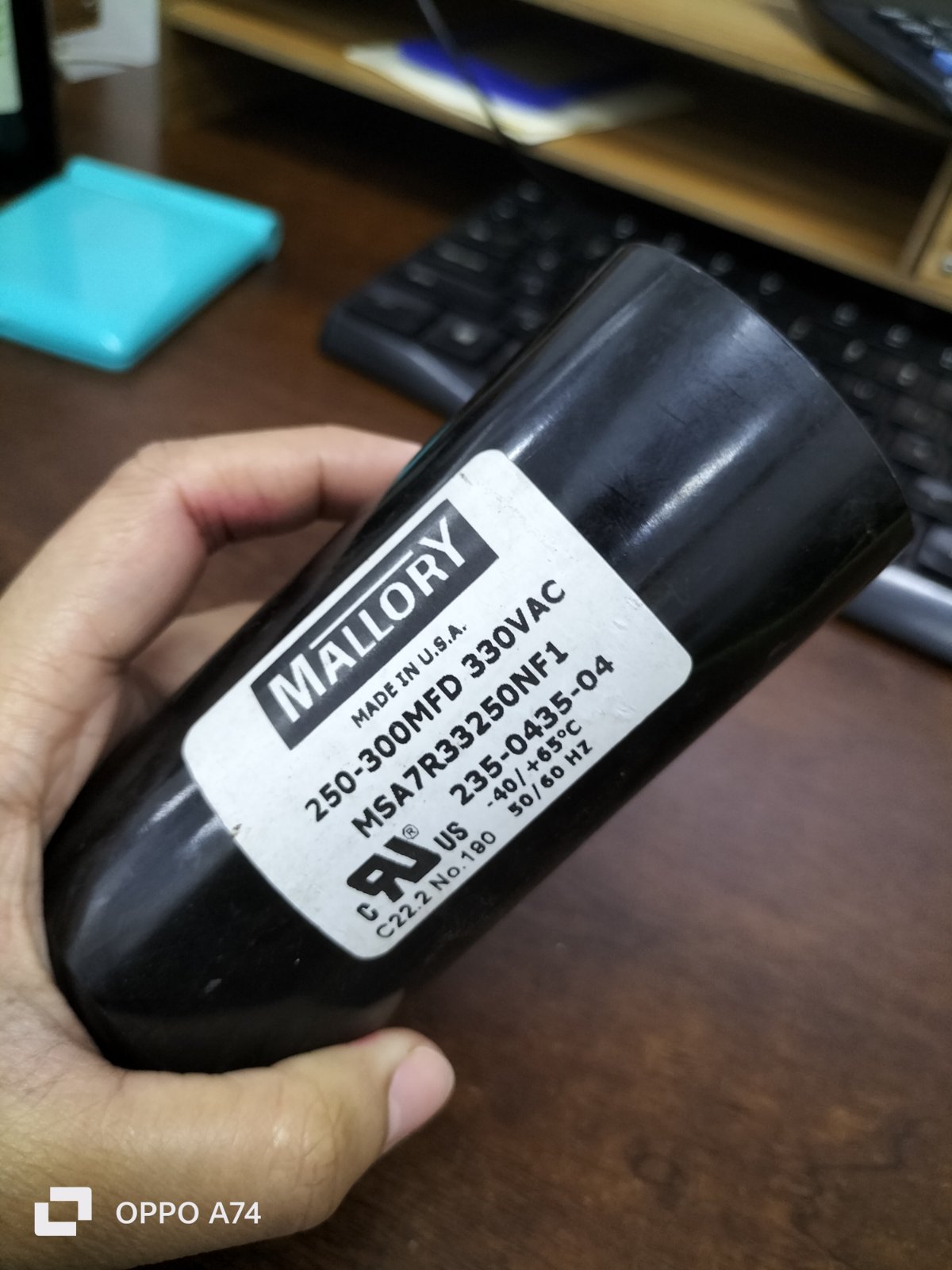 Mallory Capacitor 250-300 MFD 330 VAC electrical circuitry part held in hand on wooden desk