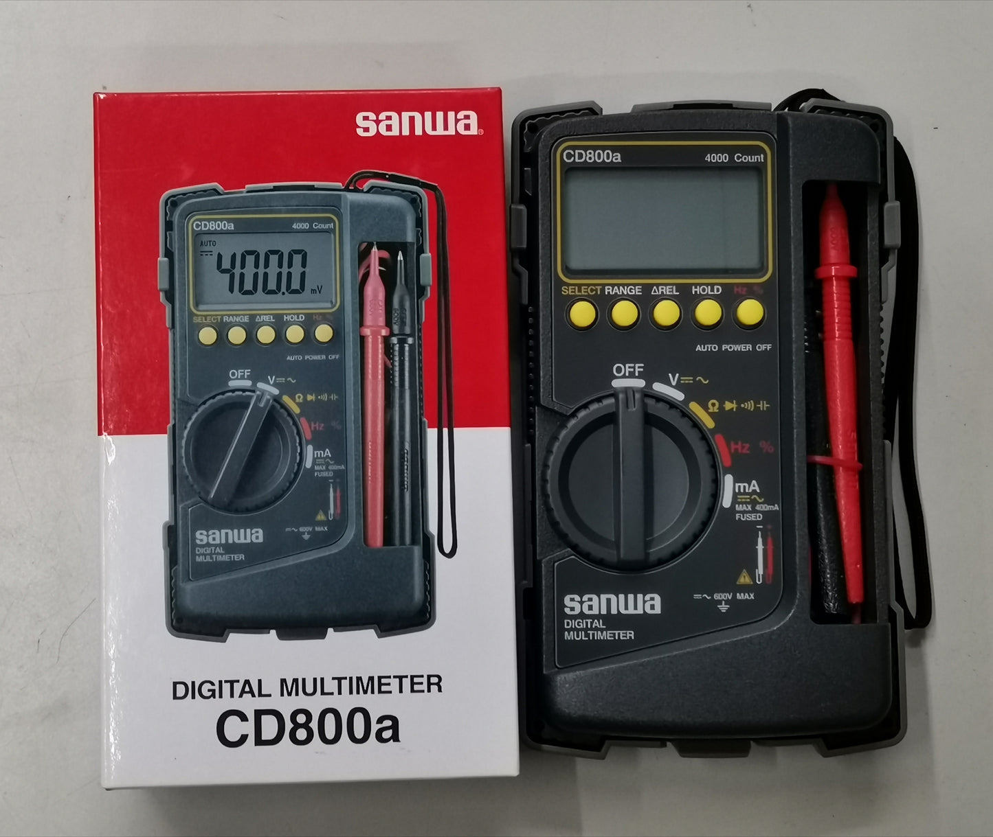 Sanwa CD800a Digital Multimeter with black body and red testing probes next to its packaging box