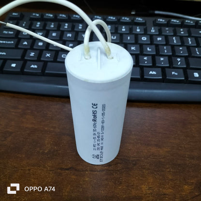 Syscap white cylindrical motor capacitor with wires on wooden desk in front of black keyboard